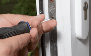 A person loosening a door hinge with a screwdriver.